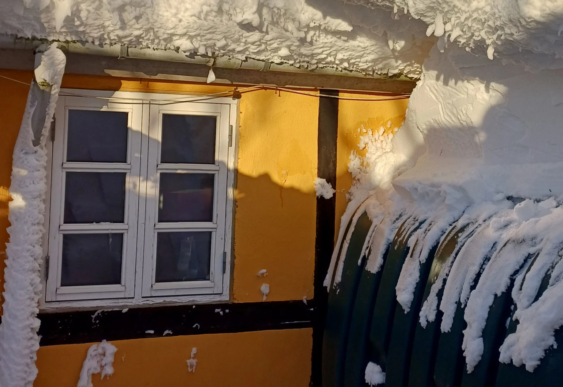 Et gult hus med en stor mængde sne på taget