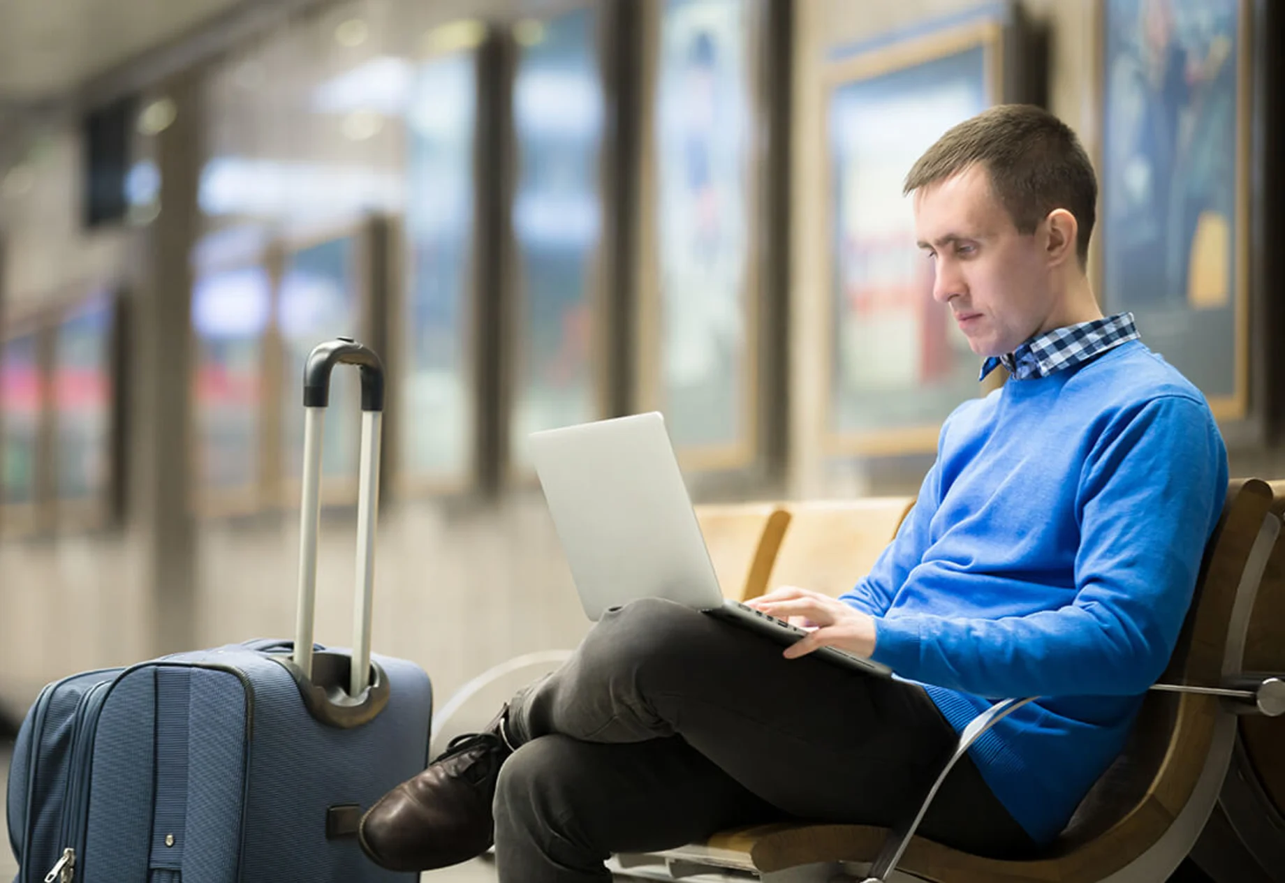 Mand som sidder på en banegård med kuffert og sin computer