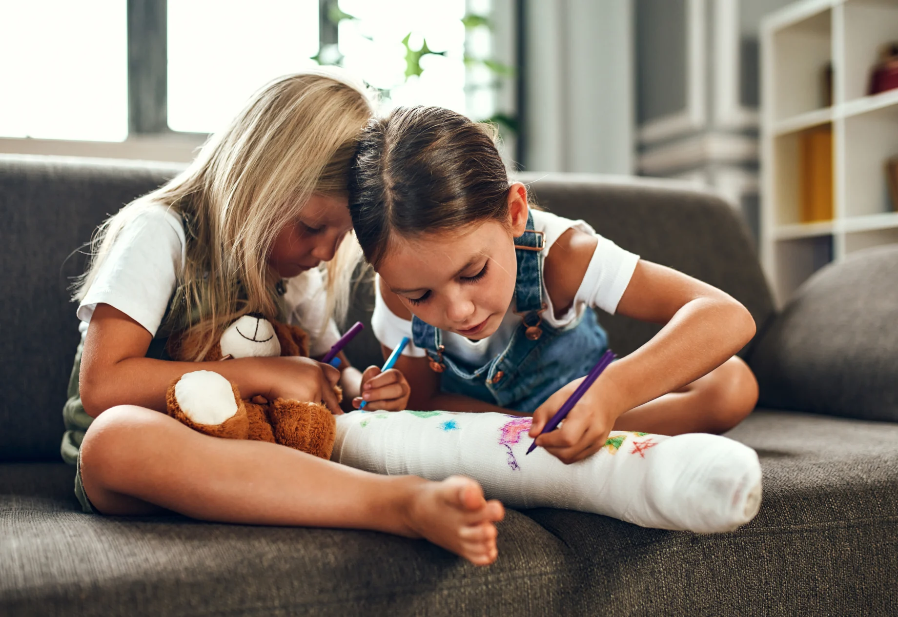 Piger som tegner på den enes gips, omkring hendes ben
