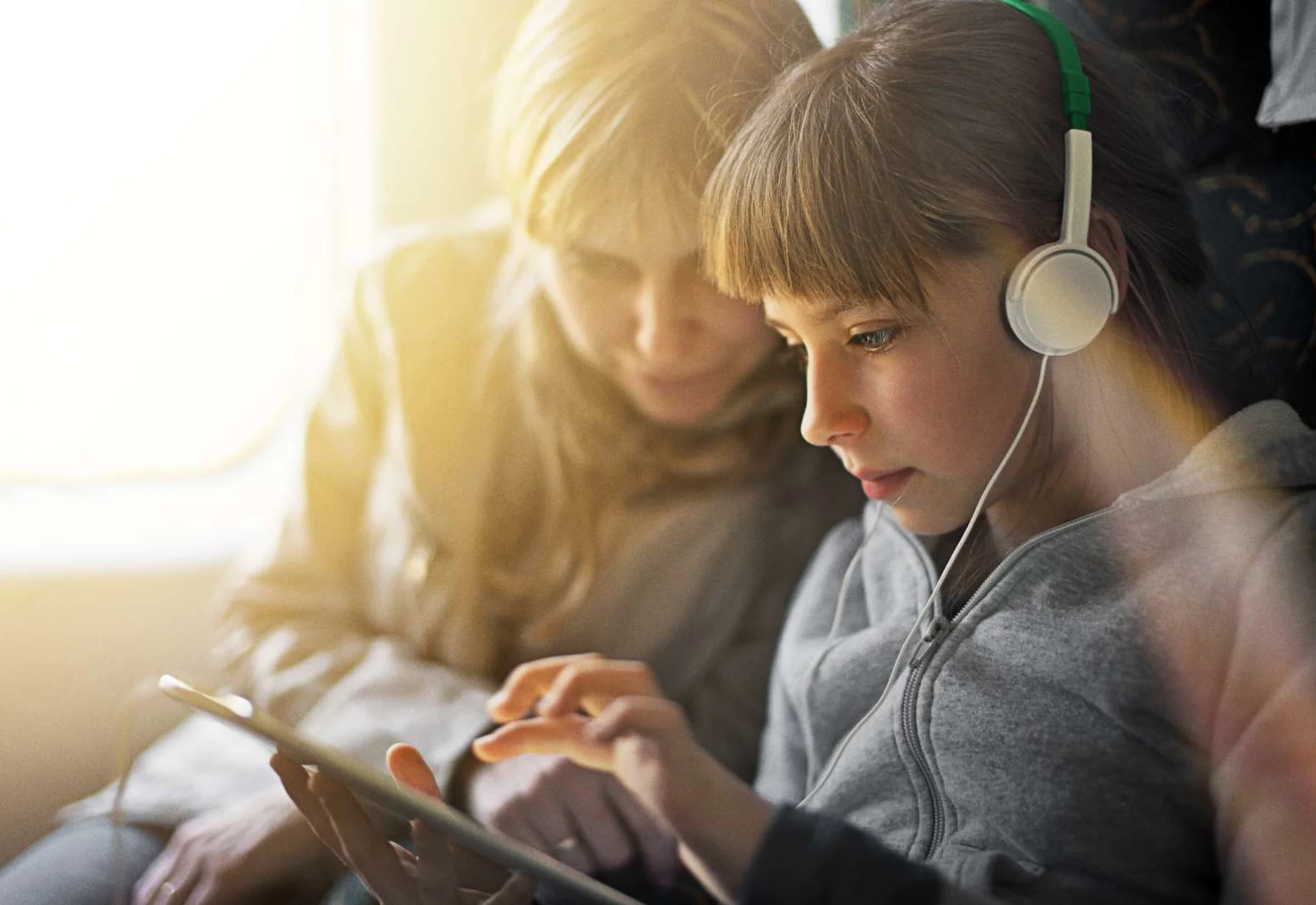 Mor og datter sidder i tog og kigger på iPad