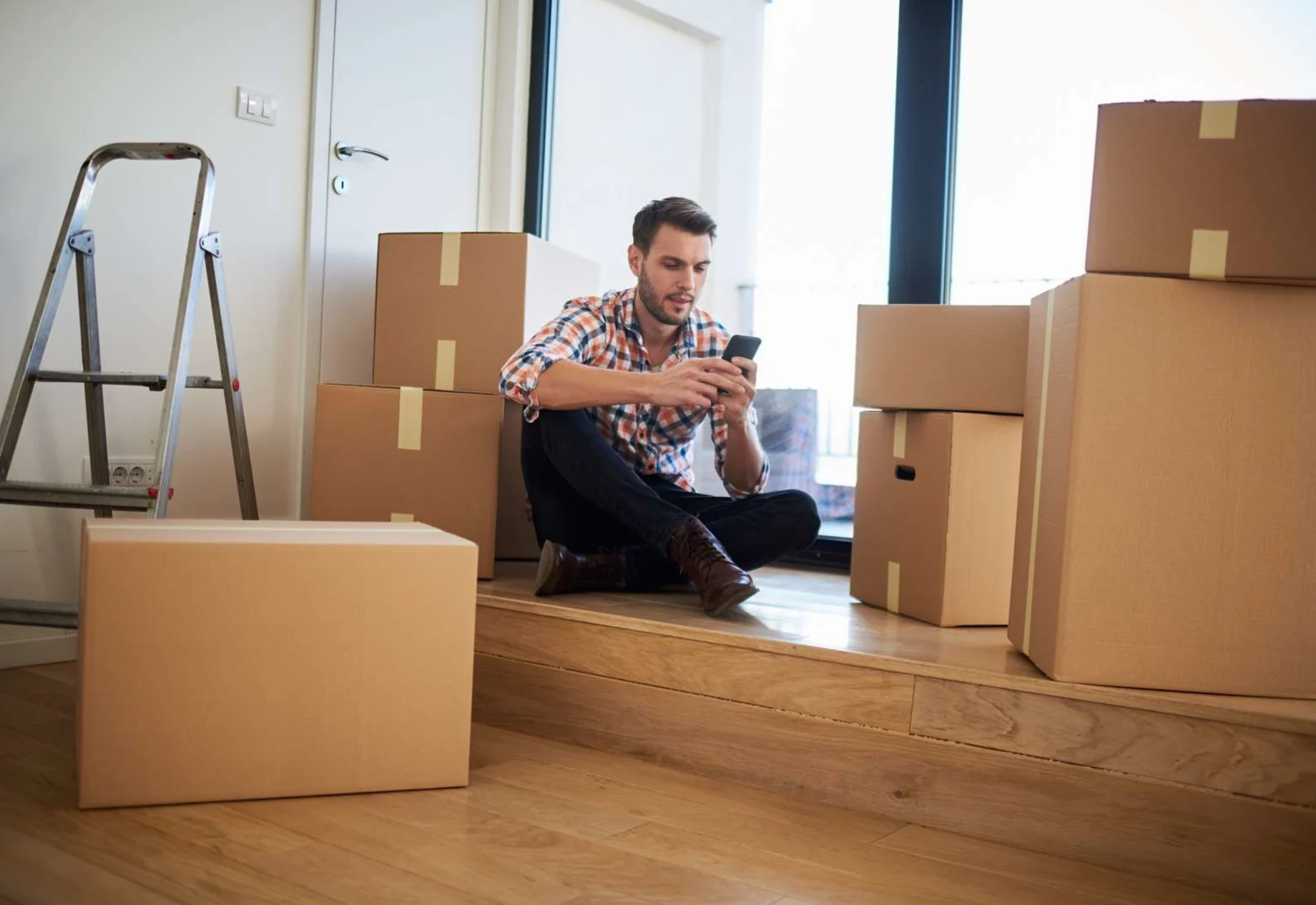 Ung mand med sin mobil blandt flyttekasser