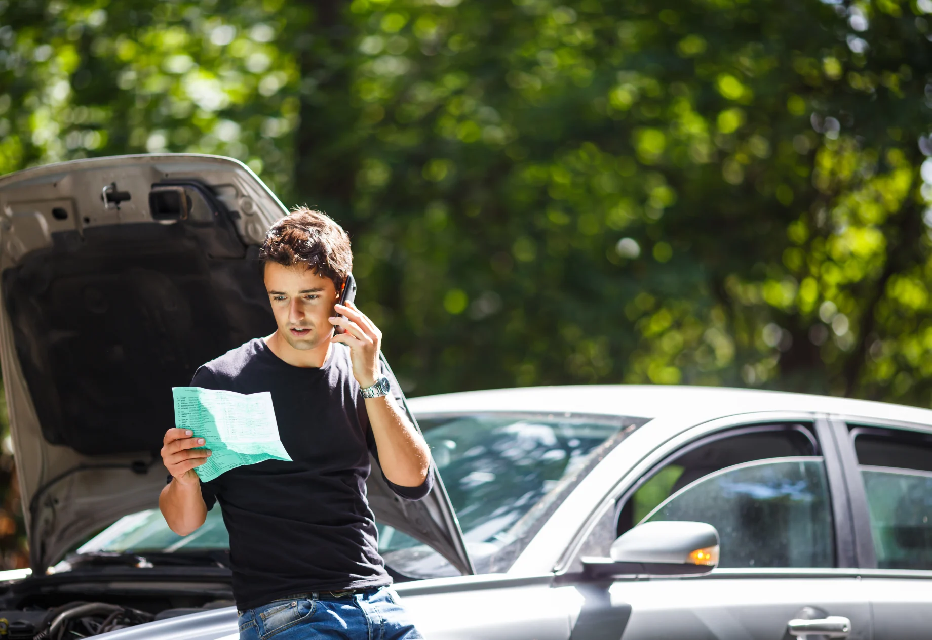 Ung mand taler i telefon mens han kigger på bil-manualen
