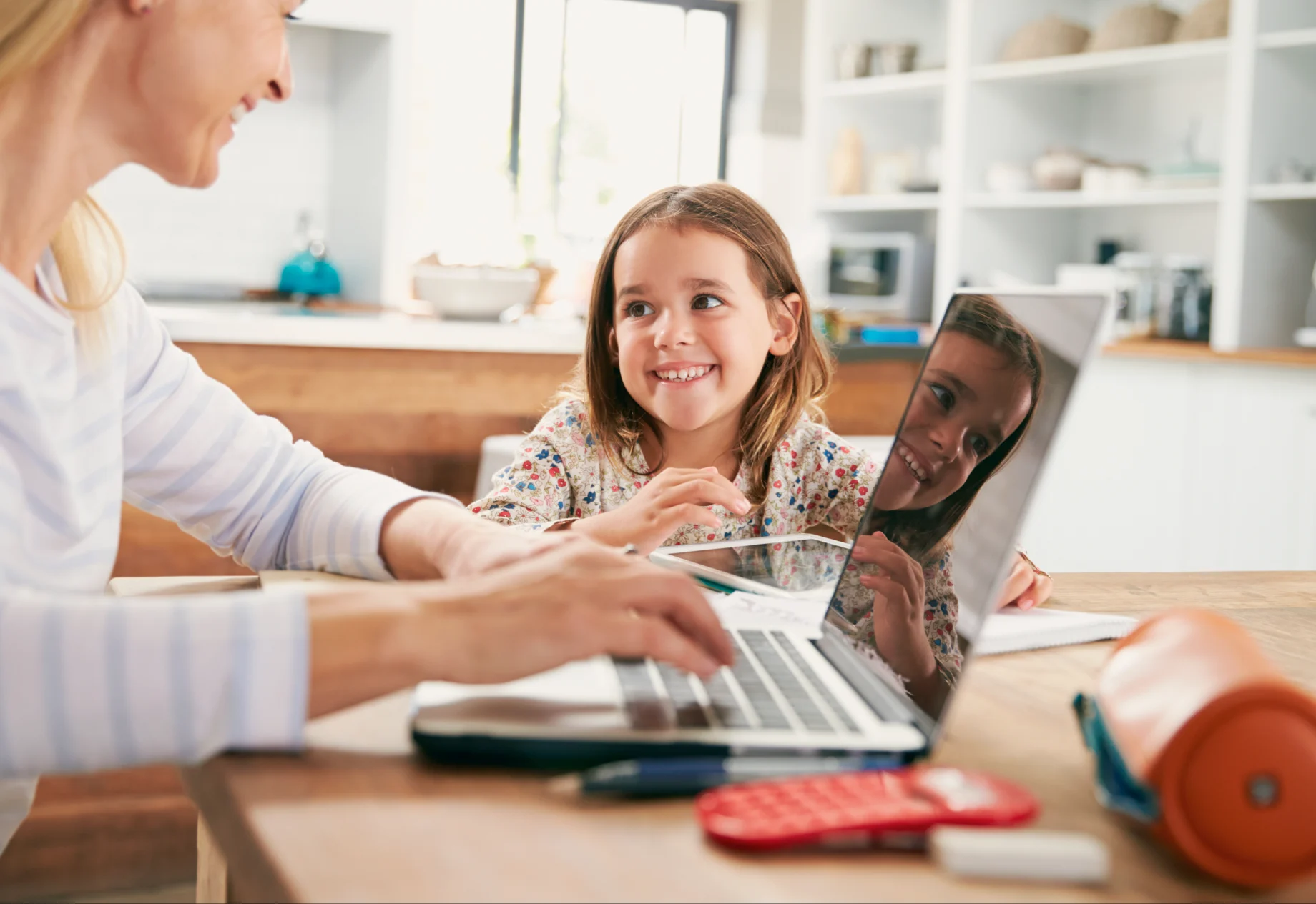 Mor og datter sidder ved spisebord sammen, og med en computer