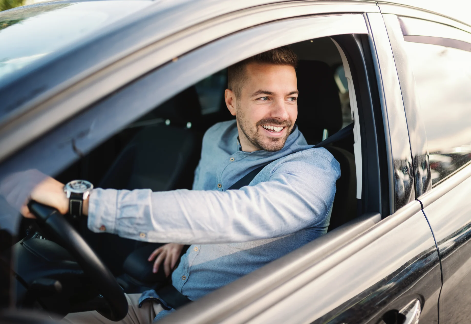 Mand som smiler bag rattet i en bil