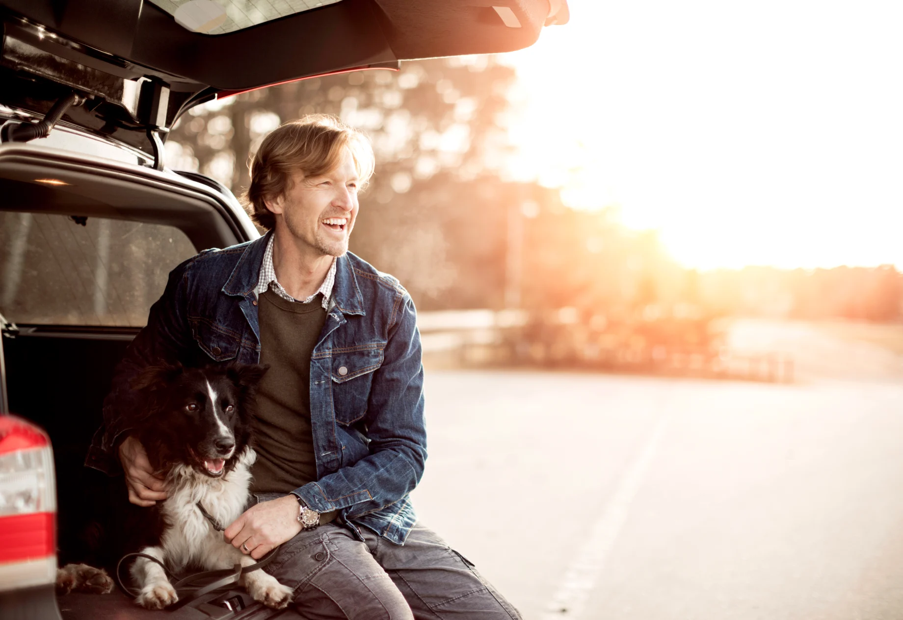 Mand sidder i bagagerummet med hans hund