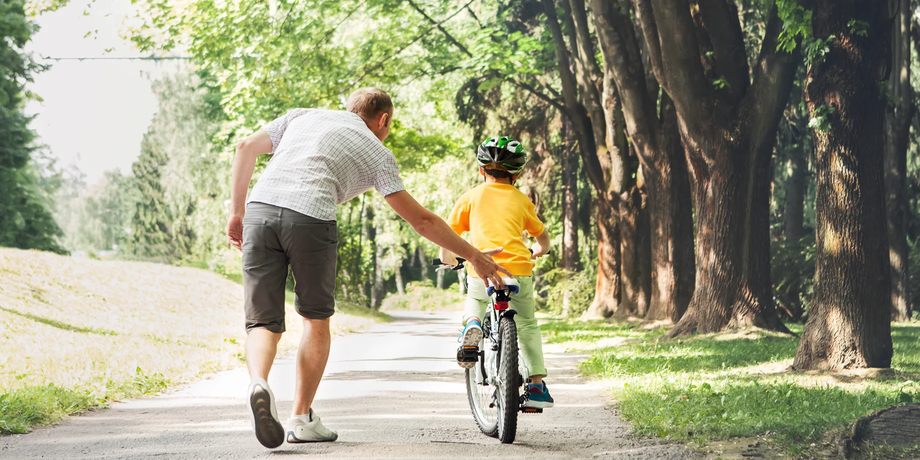 Mand som hjælper en lille dreng cykle i en skov