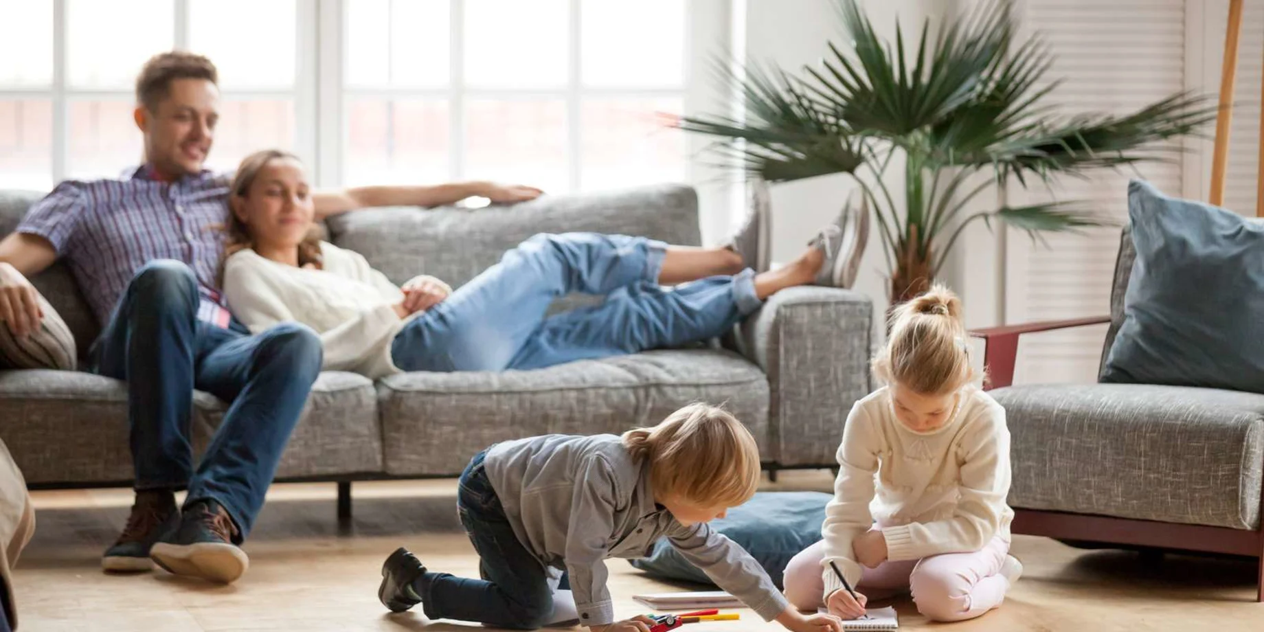 Forældre ligger i sofaen og børn leger på gulvet