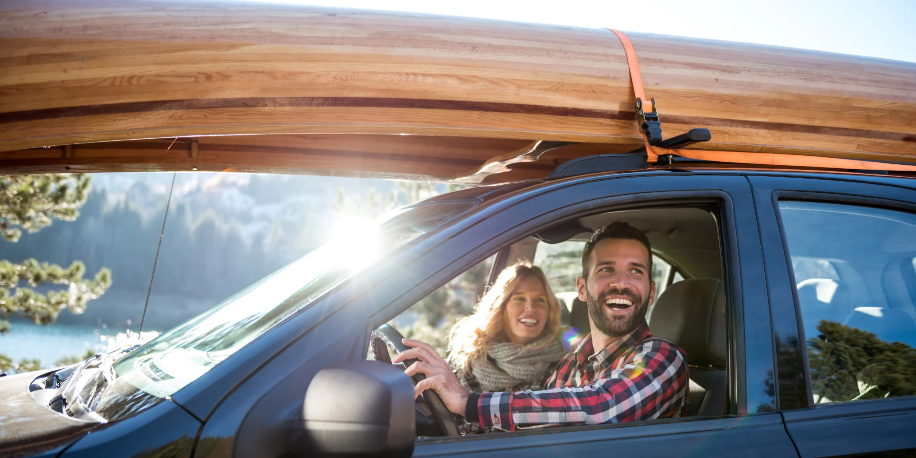 Mand og kvinde som sidder i bil. Ovenpå billedet er en kano