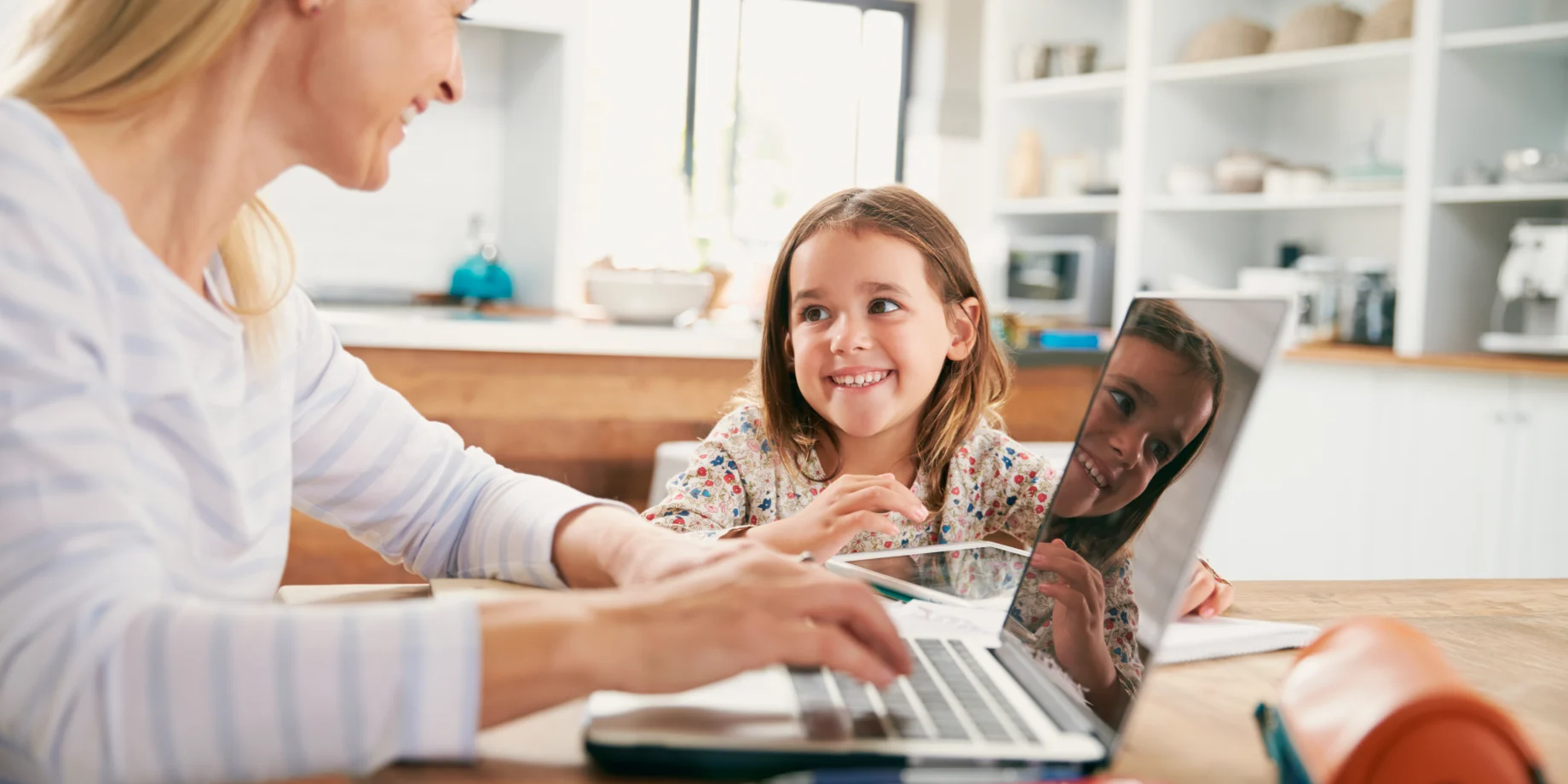 Mor og datter sidder ved spisebord sammen, og med en computer