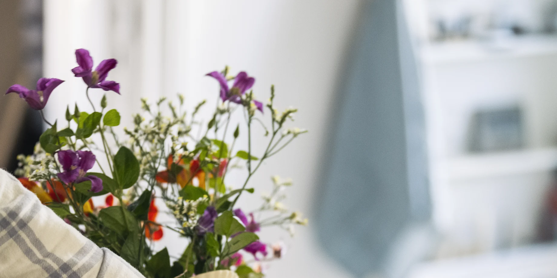 Hånd som rækker ud efter en kop med kaffe i og vælter vase med blomster i
