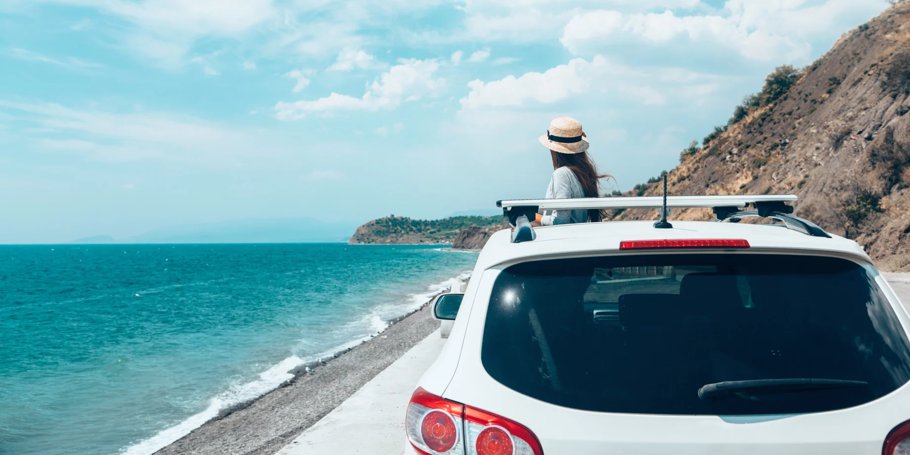 Kvinde med stråhat, som står ved vandet sammen med hendes bil